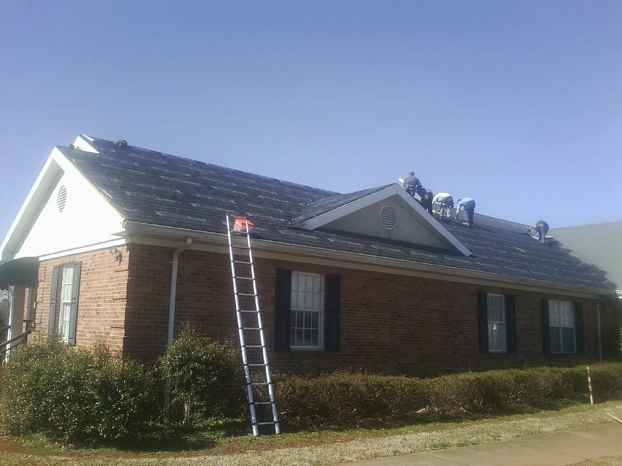 Crew tearing shingles off a brick ranch roof with a ladder set — Metal Roof Repair work by our crew in Rockland