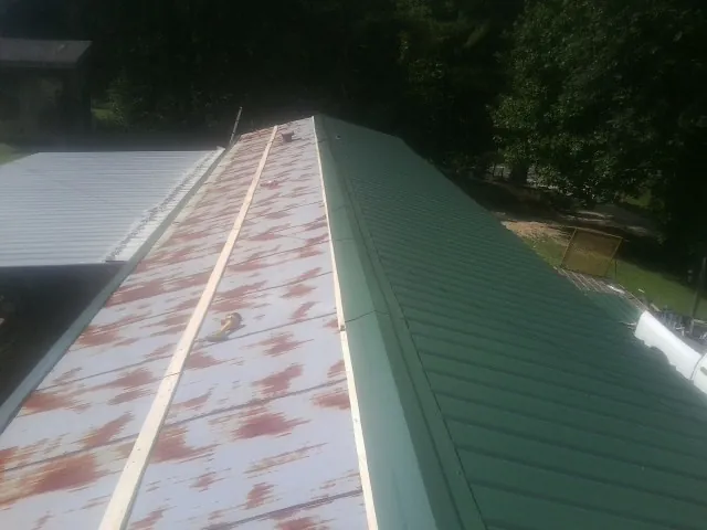 Old rusted panels beside newly installed green metal roofing — Wind Damage Roof Repair by Roofing Brothers in Rockland