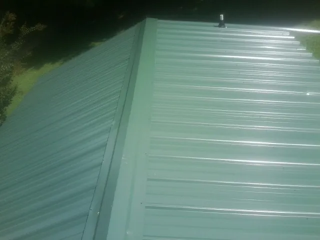 New green metal panels meeting at the ridge of a roof — Flat Roof Repair work by our crew in Rockland