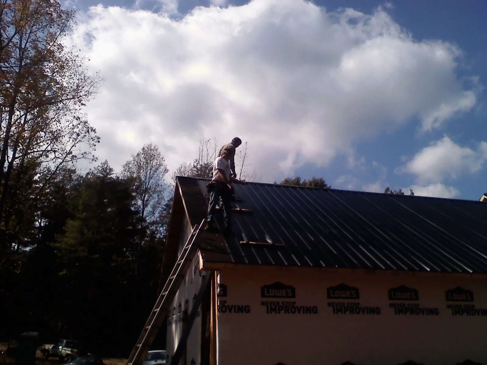 Roofer fastening dark metal panels high against a cloudy sky in Rockland