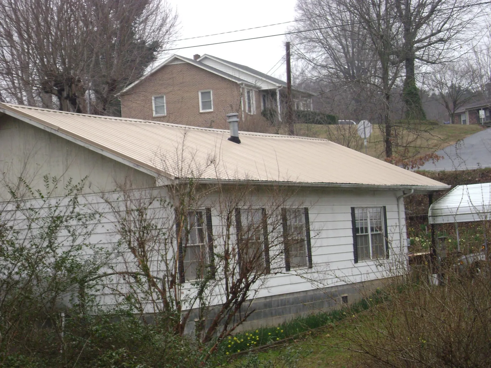 Tan metal roof on a white sided house set into a hillside — Commercial Roofing by Roofing Brothers in Rockland
